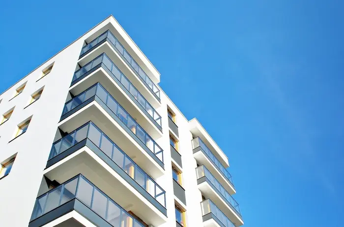 نمای بیرونی سنگی ساختمان با تراس های شیشه ای در زیر آسمان آبی صاف . قانون جدید پیش_فروش آپارتمان 4937584838