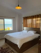 تخت خواب با روتختی سفید و پنجره رو به دریا اتاق خواب آپارتمان در سادات شهر